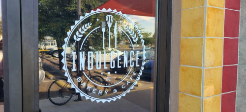 Logo of "Indulgence Bakery & Café" displayed on a glass door, featuring utensils and decorative elements.